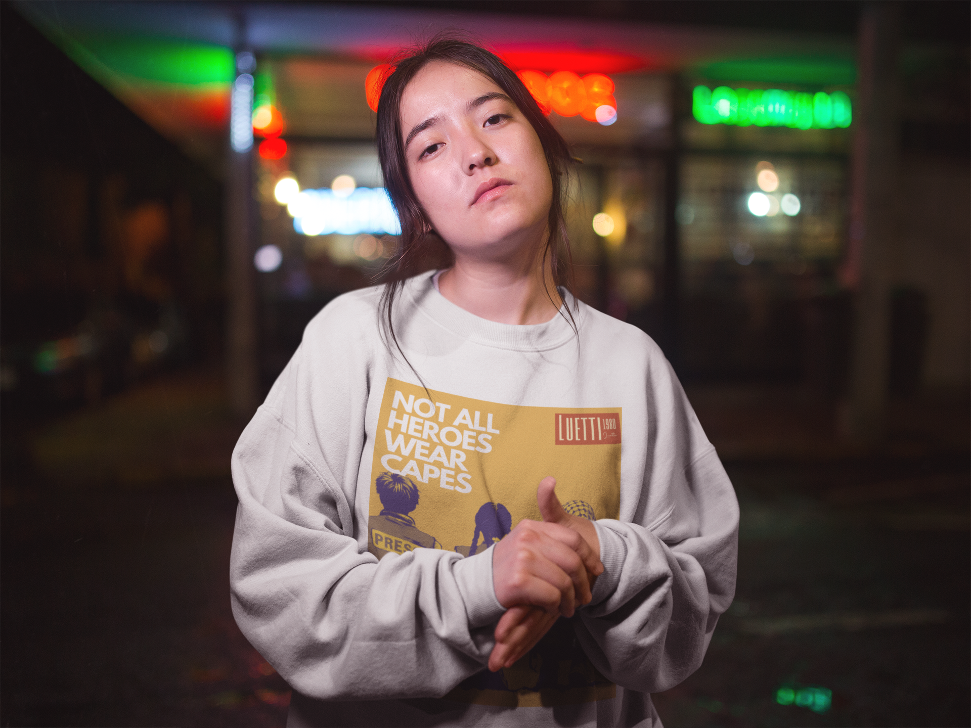 Asian girl wearing a white sweatshirt that says Not All Heroes Wear Capes with a picture of three palestinian youth wearing Press vests